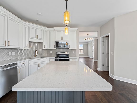 The large island provides ample counter space for meal preparation and casual dining. Pendant lighting and under-cabinet lights ensure excellent visibility and create a warm, inviting atmosphere.