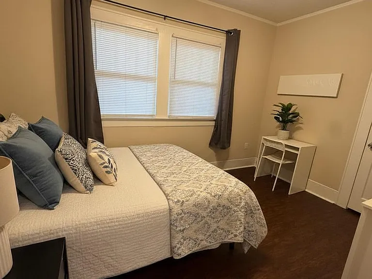 Furnished bedroom featuring a queen-size bed, closet, dresser storage and a compact desk area for work or study.