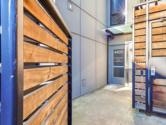 Modern exterior entrance of 4400 Alaska Apartments in Seattle, WA. Features sleek gray paneling, stylish wooden gates, and a clear entryway, enhancing urban ...