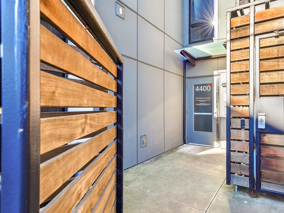 Modern exterior entrance of 4400 Alaska Apartments in Seattle, WA. Features sleek gray paneling, stylish wooden gates, and a clear entryway, enhancing urban ...