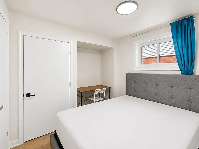 Private bedroom with a full-size bed, dedicated desk nook, and a window with curtains for natural light and privacy.