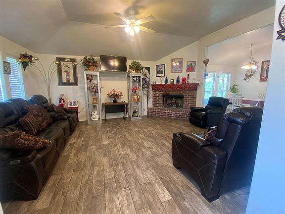 Living room with hardwood / wood-style flooring, a brick fireplace, ceiling fan, and vaulted ceiling