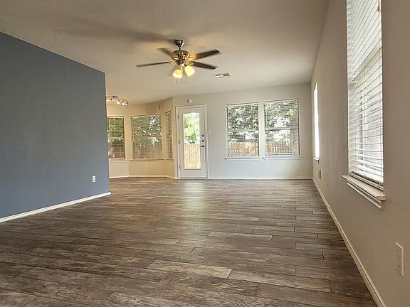 Spacious living room with elegant tile flooring, ceiling fan, and abundant natural light from large windows. Features an accent wall, open layout, and direct access to the backyard. Perfect for relaxing and entertaining.
