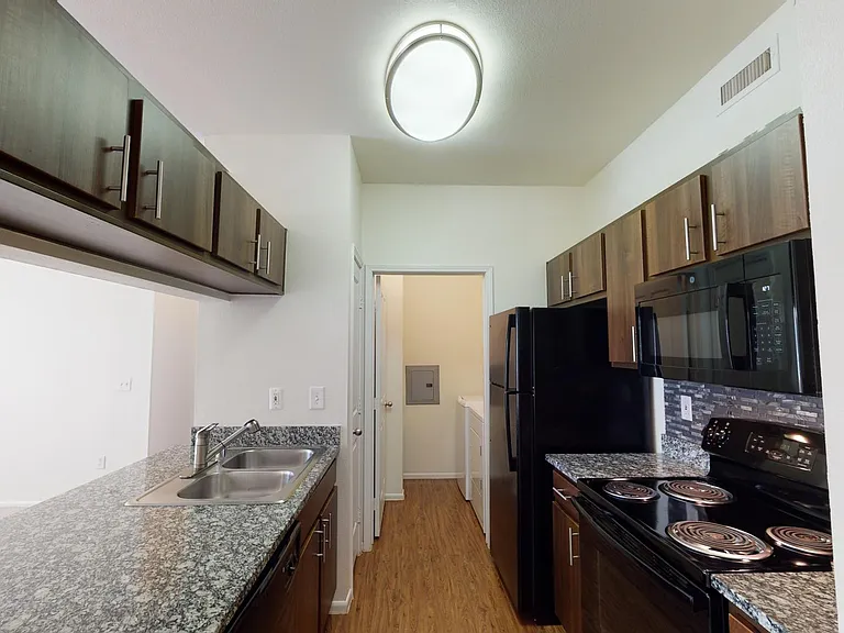 Apartment kitchen with granite countertops and wood-style flooring.