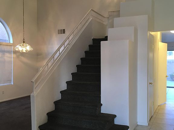 Front entry with open, vaulted ceiling and tasteful light fixtures with pot shelves next to the stairs.