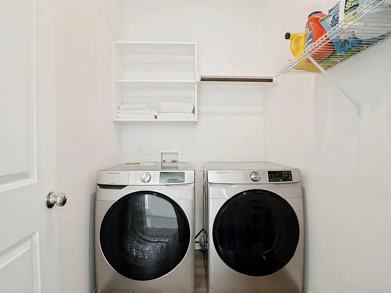 Dedicated laundry area featuring a front-loading washer and dryer, white shelving, and a hanging rod