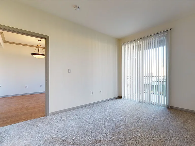 Spacious apartment bedroom with plush carpet flooring and balcony access in select homes.