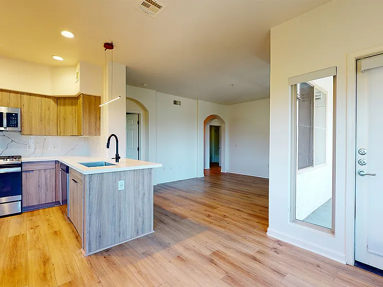 Apartment kitchen with stainless steel appliances, dining and living room with wood-style flooring.