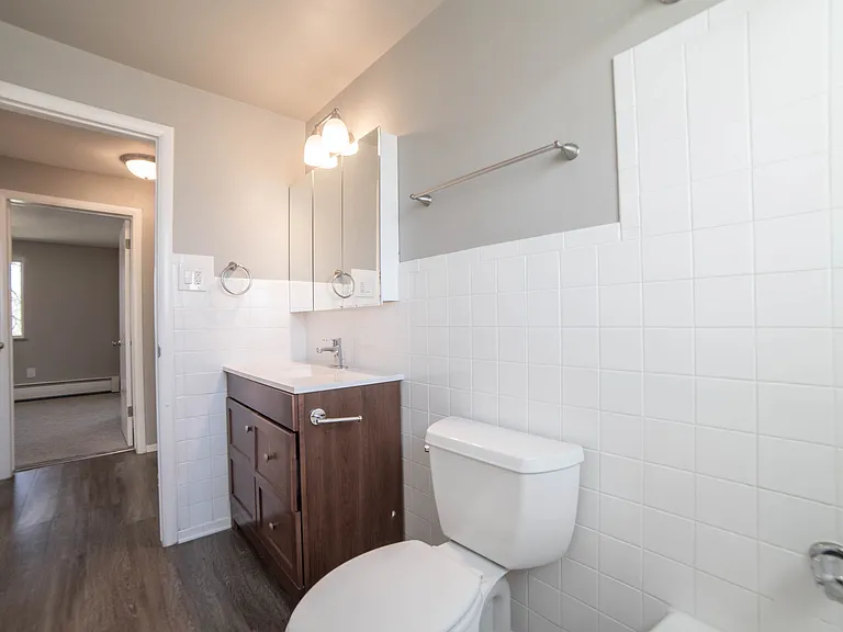 Bright and modern bathroom with elegant fixtures, a sleek wooden vanity, and pristine white tiles, offering a fresh and inviting atmosphere.