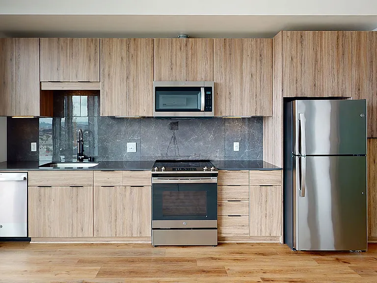 Apartment kitchen with stainless steel appliances and wood-style flooring.