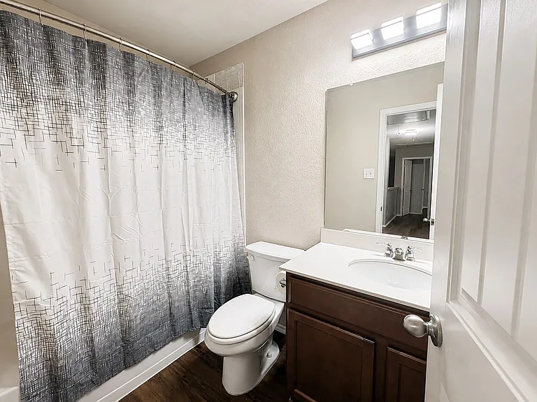 Bathroom featuring a wood-finish vanity with a white countertop and integrated sink, a large wall mirror, and a three-light vanity fixture