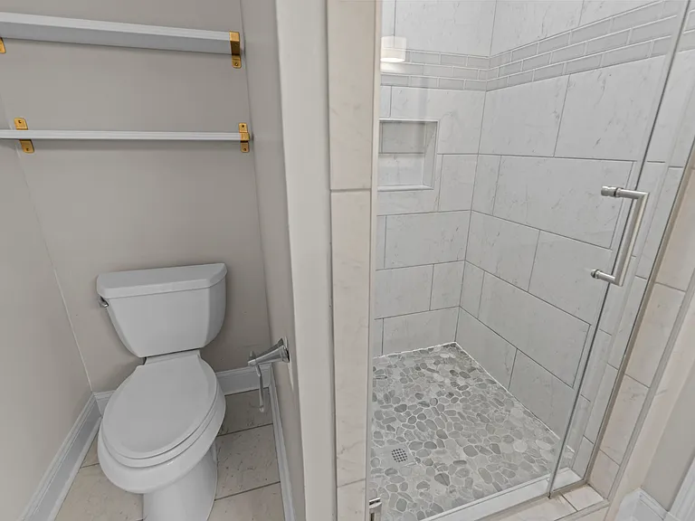 Elegant bathroom with floor-to-ceiling tile, glass-enclosed walk-in shower with pebble stone flooring, and gold accent hardware.