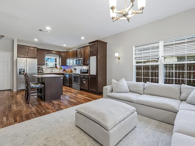 Open-concept living area featuring rich wood-finish flooring, a kitchen island with stone countertop, stainless steel appliances, and a tiled backsplash