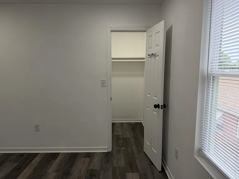 Unfurnished room with wood-look flooring, a window with blinds, and an open closet for convenient storage.