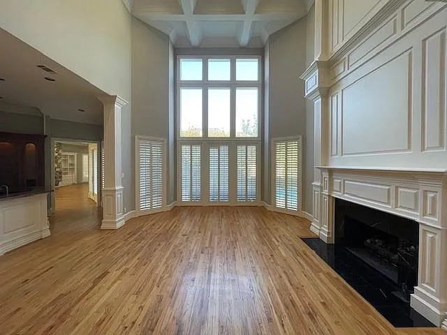 Unfurnished living room featuring a fireplace, light wood-type flooring, coffered ceiling, a high ceiling, and beam ceiling