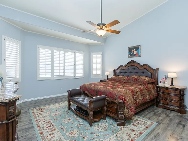 Very spacious primary suite or master bedroom featuring vintage oak wood-look flooring, vaulted ceilings & window wood shutters