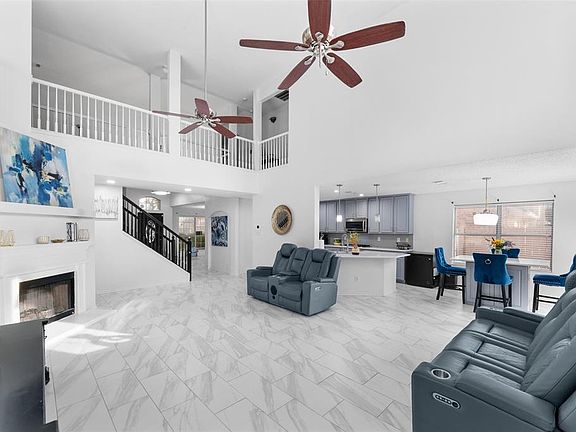 Living area featuring a fireplace with raised hearth, stairs, a ceiling fan, light marble finish flooring, and a high ceiling