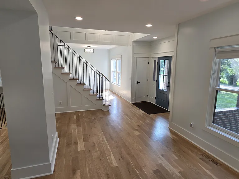 View from living area of stair case, front door, coat closet with dining room in background.