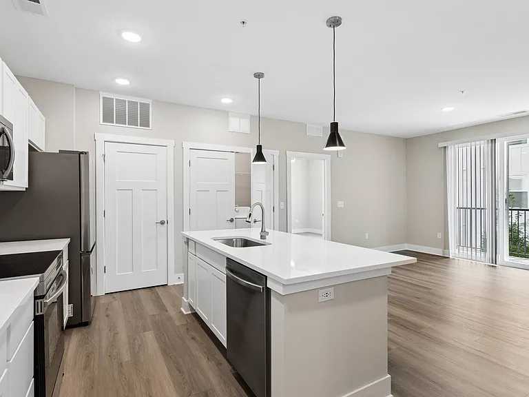 Kitchen with quartz countertop, refrigerator, stove, oven, dishwasher, and microwave, and the living area, of an apartment unit at Tiffany Flats in Columbus, OH.