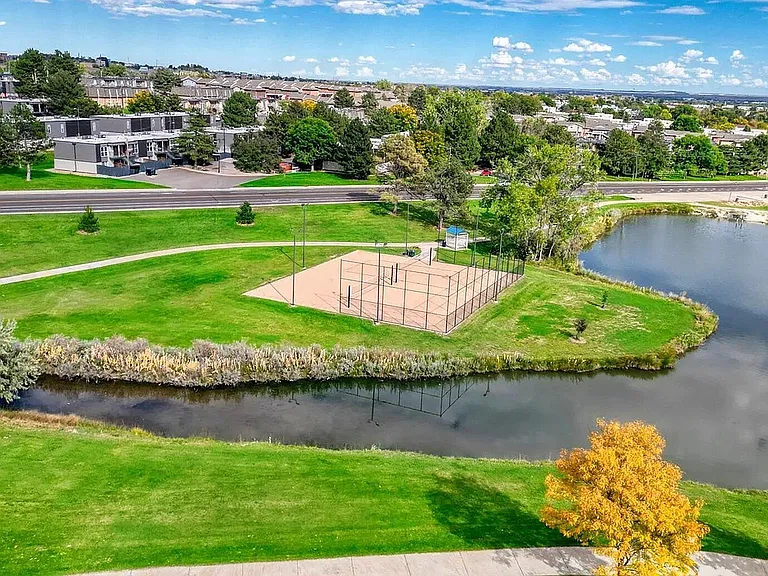 Scenic aerial view of a vibrant community park with a charming pond, lush greenery, and a fenced sports court, perfect for outdoor activities and relaxation.