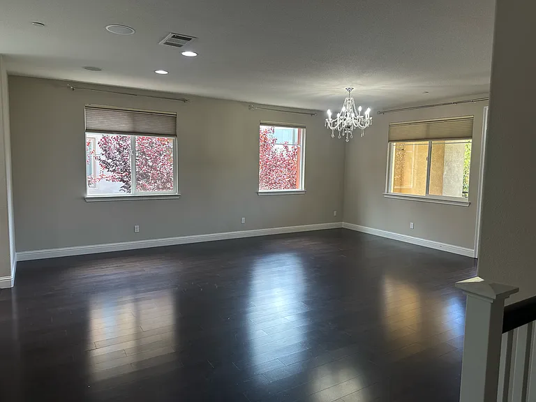 Open living room with rich hardwood floors, stylish chandelier, and multiple large windows letting in abundant light.