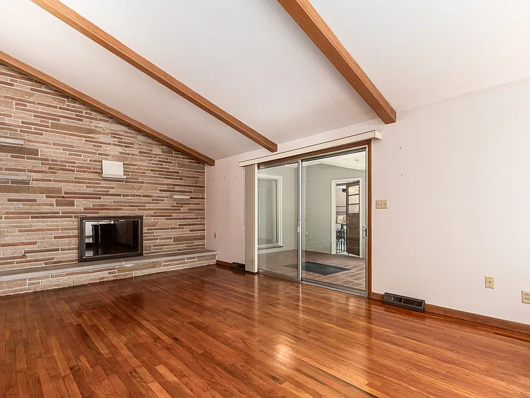 Living room view with pristine natural hardwood floors, natural stone accent wall with a wood burning fireplace. Additional access to the sunroom