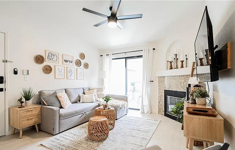 Open living area features a sectional seating setup, ceiling fan, and a fireplace with mantle, plus sliding-door access to th