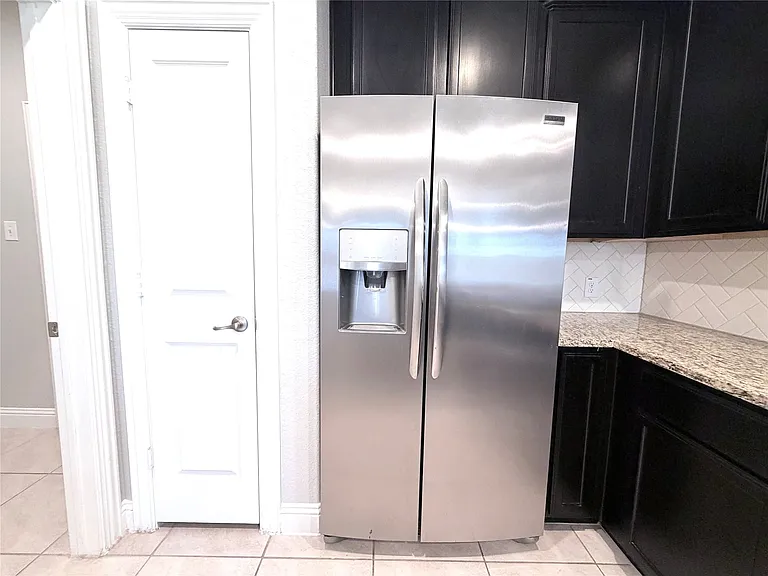 This spacious, modern kitchen is highlighted by high-end stainless steel side-by-side refrigerator appliances complete with integrated ice and water filtration dispensers. The room is further elevated by sophisticated espresso-toned cabinetry paired with 
