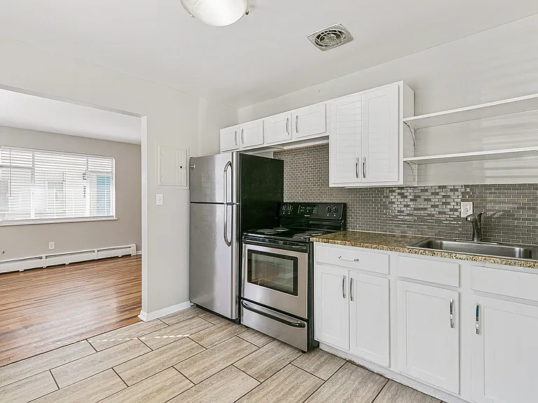 Bright, modern kitchen with stainless steel appliances, elegant tile flooring, and an open-concept view into the sleek hardwood living area.