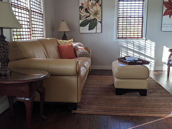 Living room has wood floors, a coat closet, Leather couch and chair, flat screen smart tv with roku and internet service, A desk area.