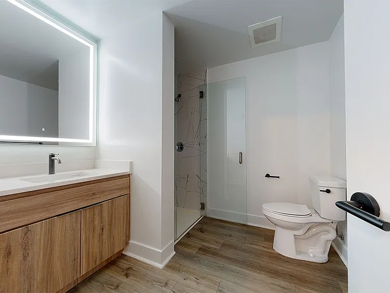 Apartment bathroom with glass enclosed shower, wood-style flooring, double sinks, and LED vanity mirror.