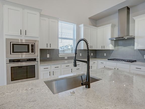 Upgraded kitchen with a tiled backsplash, white cabinetry, and oversized island.