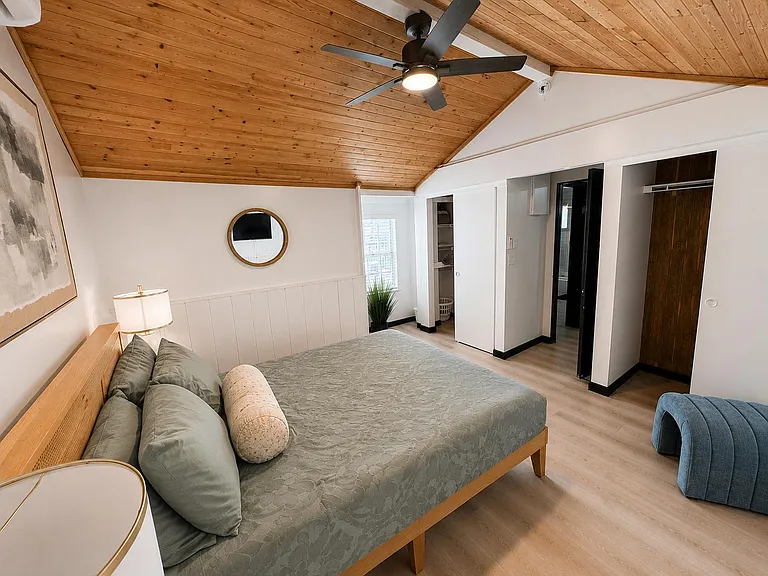 Spacious bedroom with vaulted wood ceiling, ceiling fan, and a large bed area plus open closet/storage nook.