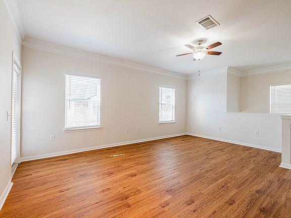 Bright and spacious living area with elegant wood-style floors, featuring large windows and a modern ceiling fan. Bright and spacious living area with elegant wood-style floors, featuring large windows and a modern ceiling fan.