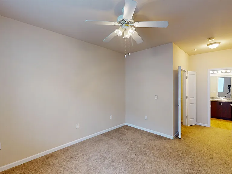 Spacious apartment bedroom with large closet, attached bathroom and plush carpet flooring.