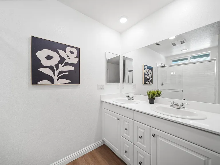Spacious bathroom vanity with double sinks, ample cabinet storage, and a large wall mirror beside a tiled tub/shower.