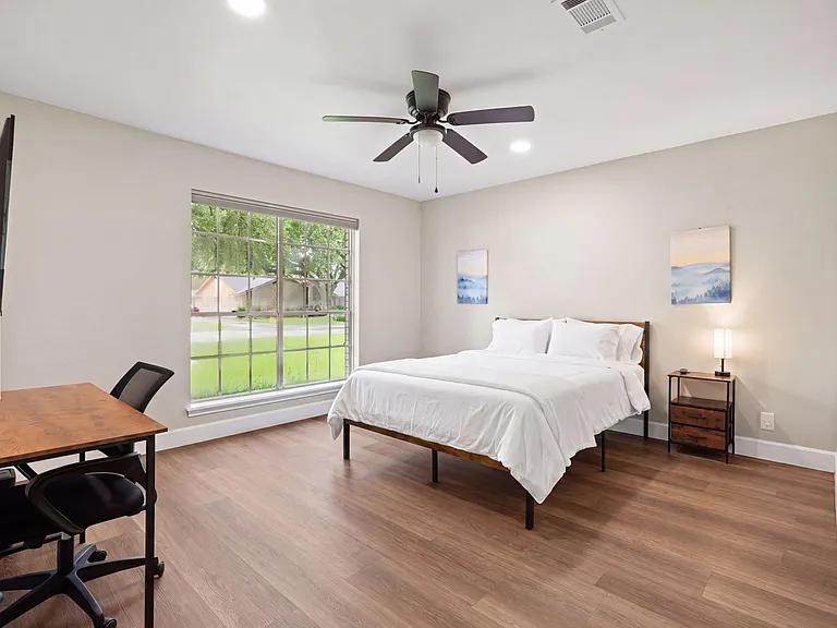 Spacious bedroom with a large window, ceiling fan, and dedicated work desk, plus a nightstand for convenient storage.
