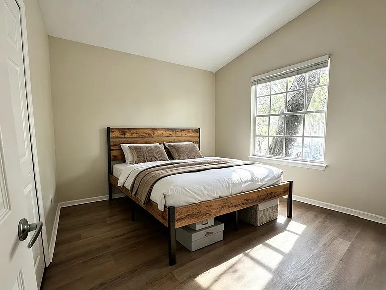 Private bedroom with a full-size bed, wide window with blinds, and durable wood-look flooring for easy upkeep.