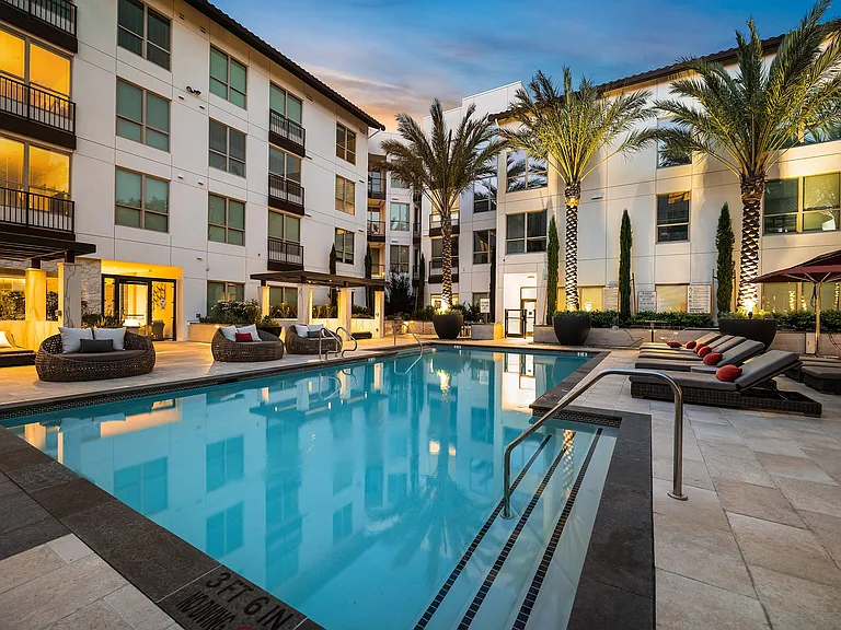 Pool with lounge seating, cabanas, and softly lit palm trees