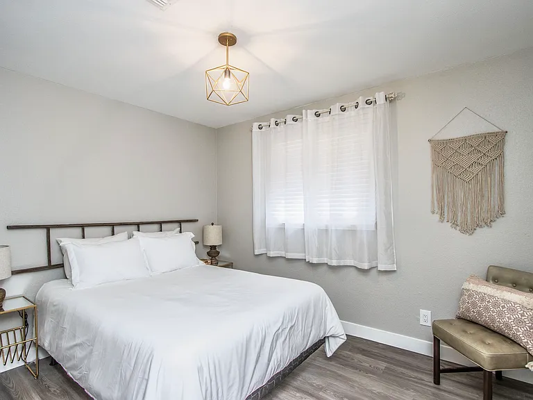 Stylish second bedroom at Casa Del Sol, Tempe rental home. Features a comfortable bed with unique wood rail headboard, gold geometric pendant light, macrame wall hanging, and a chic accent chair. Ideal cozy retreat for a top Tempe, AZ vacation stay.