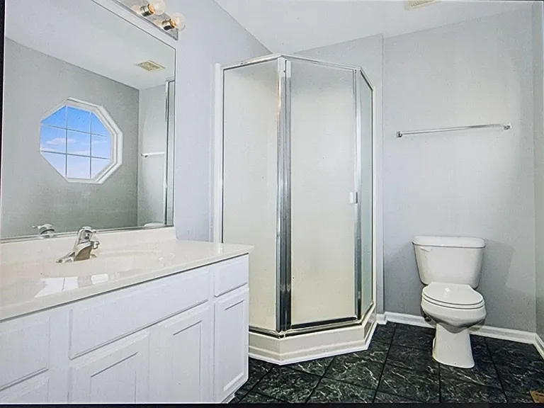 Full bathroom with a single-sink vanity, large mirror, and corner glass shower, plus an octagonal window for natural light.