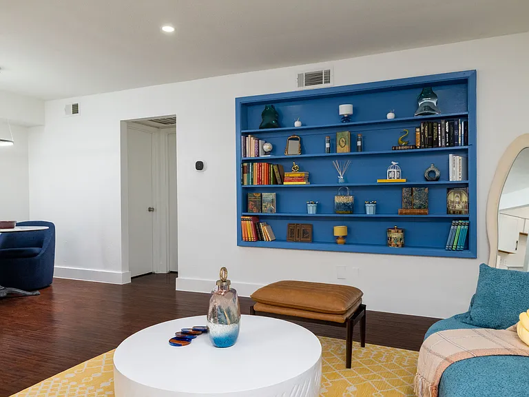 Relax in a bright and stylish living room featuring cozy blue seating, warm accents, and a modern round coffee table. Perfect for lounging, reading, or gathering with friends.