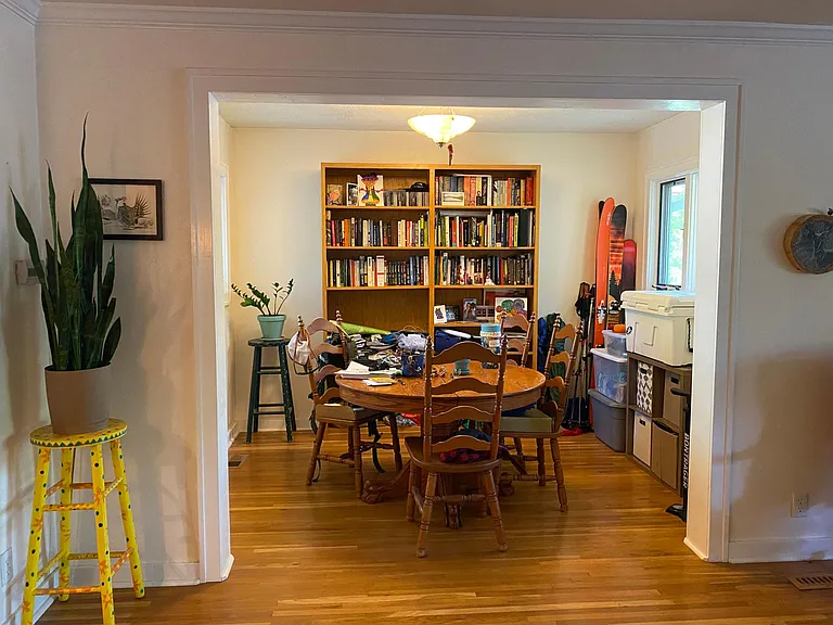 April 2025-Dining area with matching large windows on left and right. Original wood flooring throughout. Book cases and table and chairs stay with house.