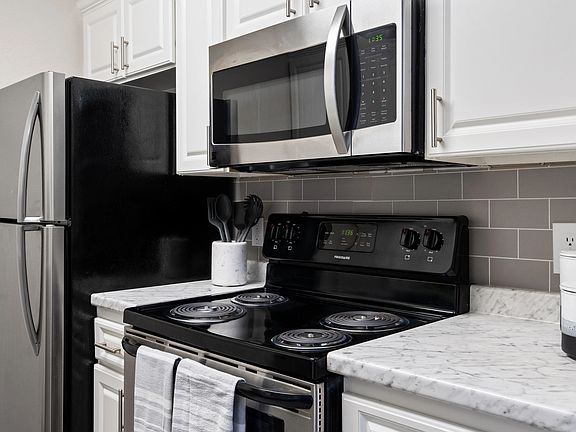This modern kitchen featuring stainless steel appliances, elegant white cabinetry, and a sleek subway tile backsplash is perfect for home cooking and entertaining.