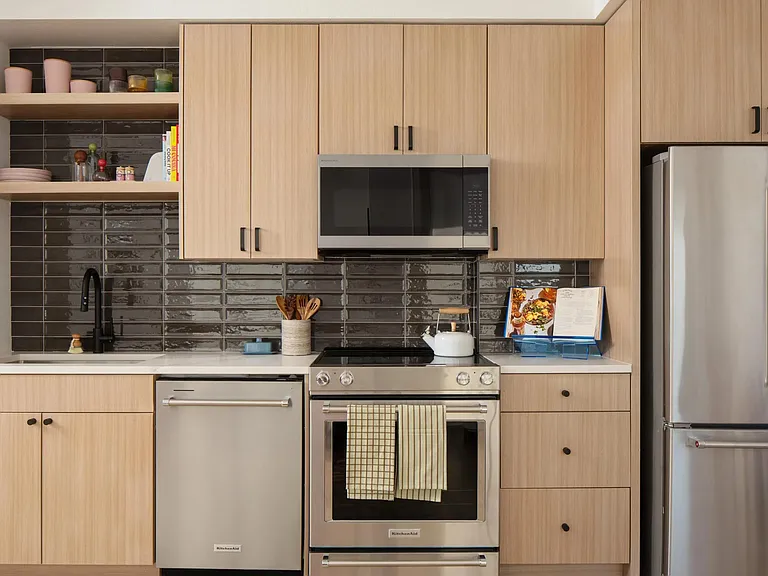 Light wood cabinetry, sleek stainless appliances, and a glossy tile backsplash create a clean, contemporary kitchen with character.