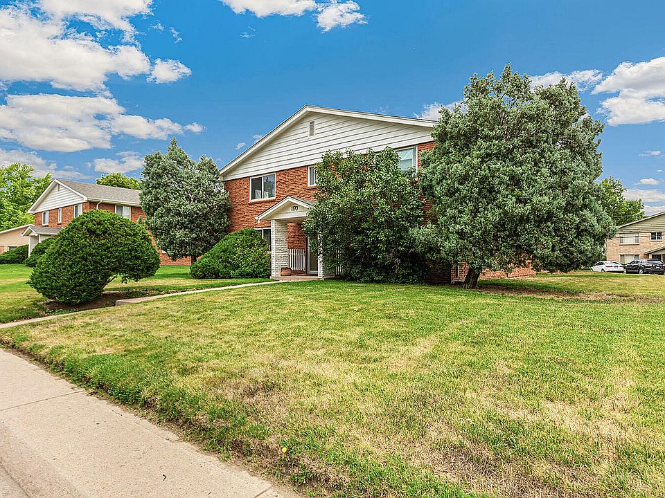 Charming brick apartment building with lush greenery and a manicured lawn under a bright blue sky.