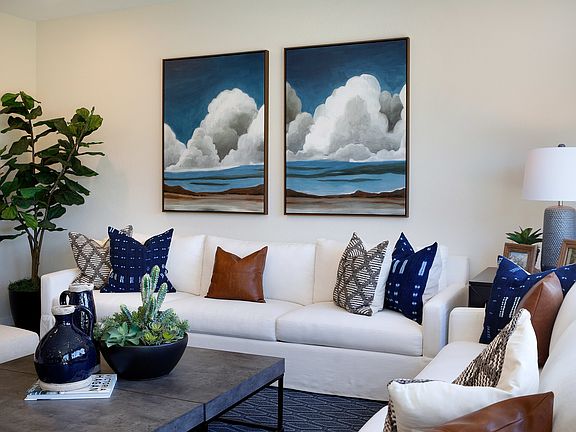 A modern and cozy living room with a large white sofa, a leather armchair, and two framed paintings