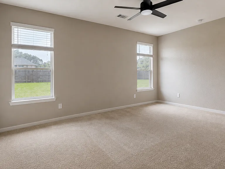 Spacious main bedroom with a ceiling fan and three large windows bringing in natural light