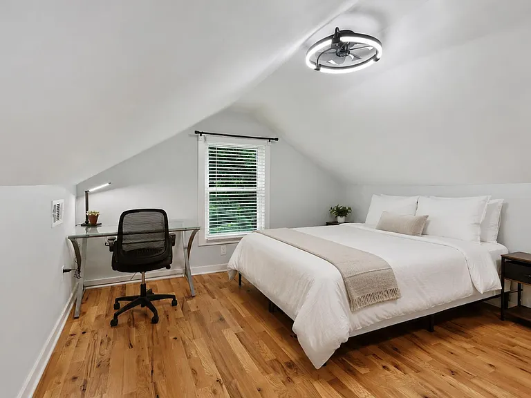 Upper-level bedroom with vaulted ceilings, hardwood floors, a desk workspace, and a window with blinds for natural light.