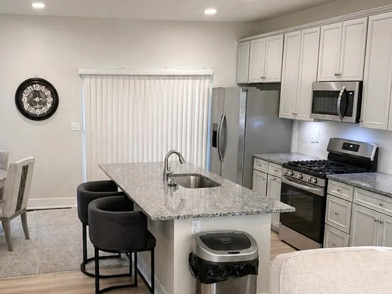 Open kitchen features a granite island with breakfast seating, stainless appliances, and ample white cabinetry for storage.
